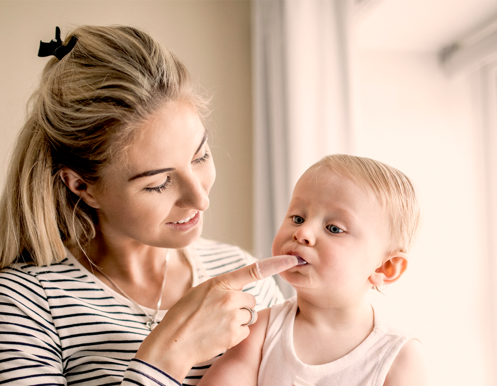 Mama putzt Baby die Zähne mit Fingerzahnbürste